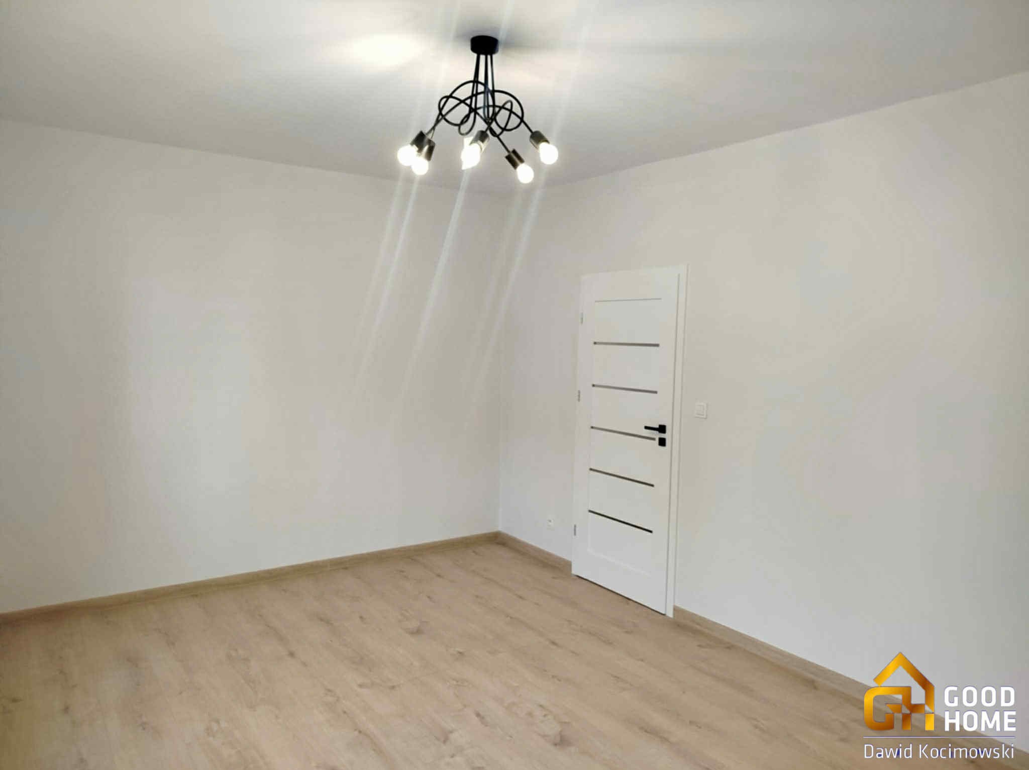 Jasny pokój po remoncie: panele podłogowe, białe ściany i drzwi z minimalistycznym designem. Nietypowa lampa sufitowa dodaje charakteru.