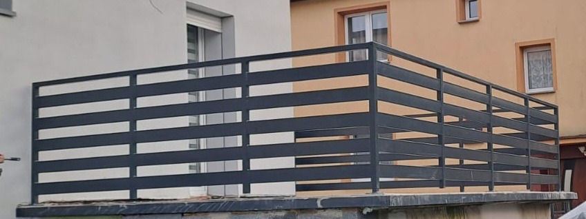 Nowoczesna, pozioma, metalowa balustrada w kolorze grafitowym, zamontowana na balkonie. Widok z zewnątrz, na tle elewacji budynku z oknami.