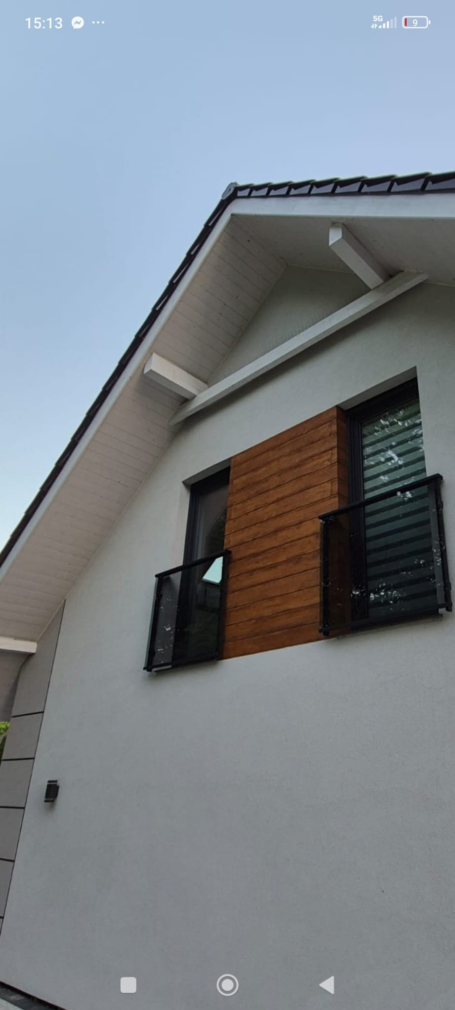 Nowoczesna balustrada szklana na balkonie domu z drewnianą elewacją. Czarne ramy, minimalistyczny design, jasna elewacja budynku.