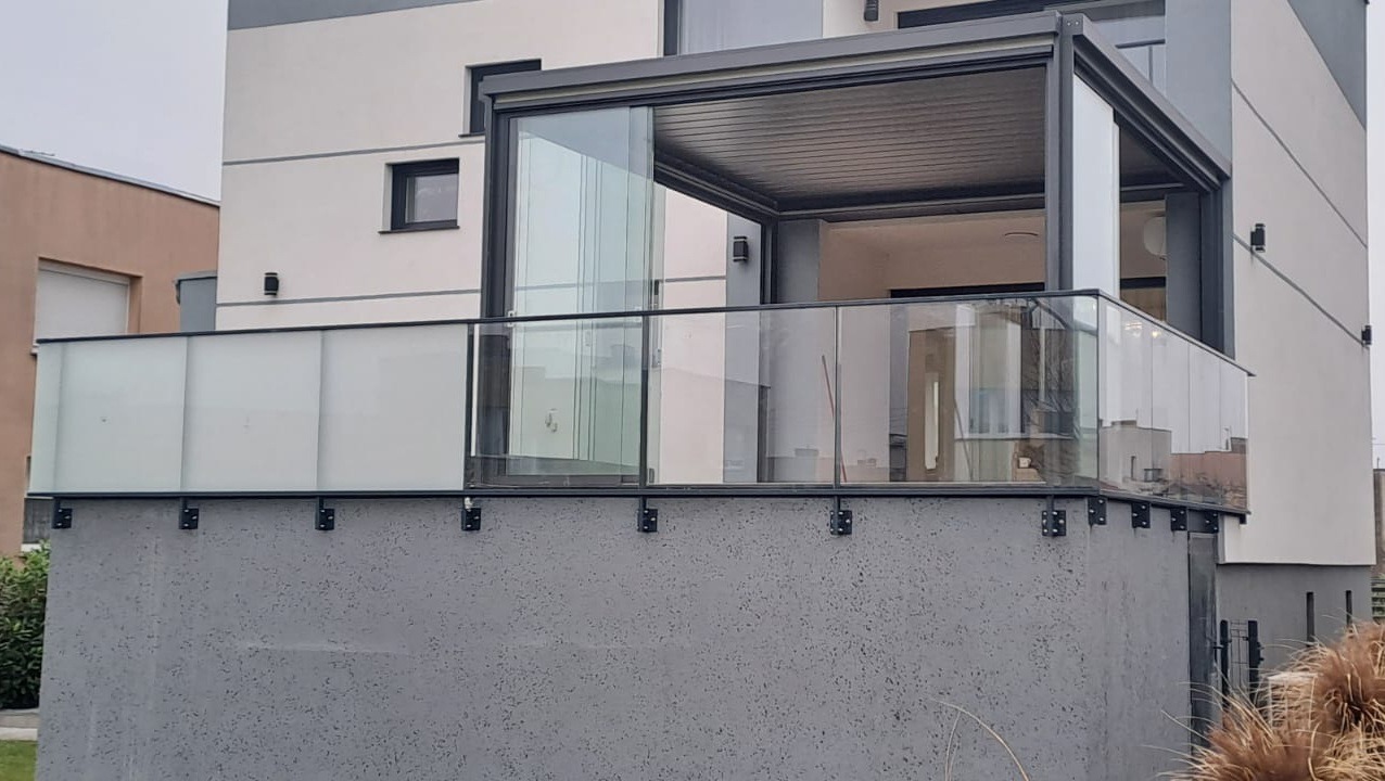 Szklana balustrada balkonowa z zadaszeniem w Wysocku. Nowoczesny design, szare elementy konstrukcyjne, widok z dołu na balkon.