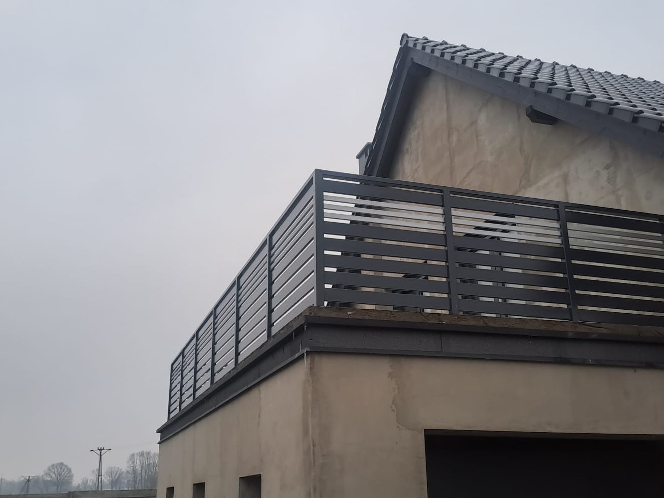 Nowoczesna, pozioma balustrada metalowa w kolorze grafitowym na balkonie domu jednorodzinnego. Widok z dołu, pochmurne niebo w tle.