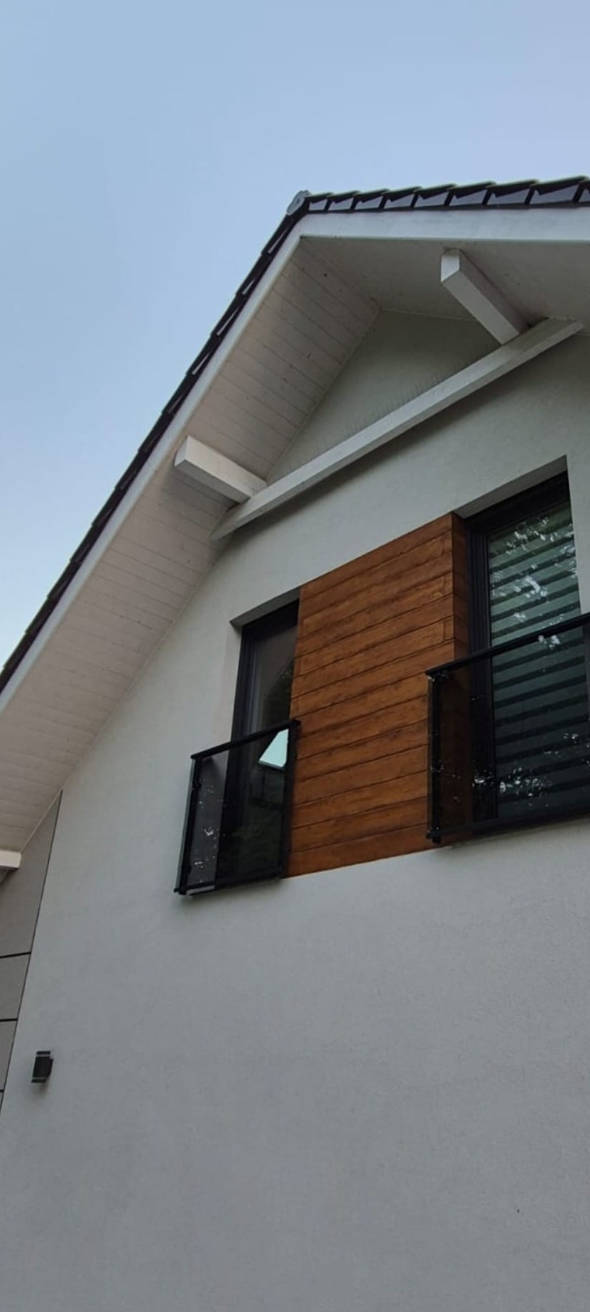 Nowoczesny dom z balkonami zabezpieczonymi szklanymi balustradami z czarnymi ramami. Elewacja w odcieniach bieli i brązu. Ujęcie z dołu.