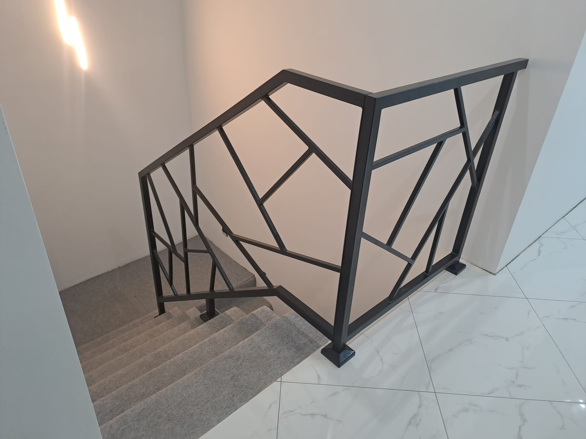 Nowoczesna, geometryczna poręcz schodowa w kolorze grafitowym, wykonana w Wysocku. Minimalistyczny design, białe ściany i marmurowe płytki podłogowe.