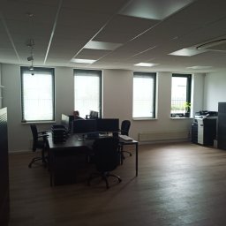 Mariusz Markowski - Przestronne biuro z trzema oknami z żaluzjami, ciemnymi biurkami z monitorami i czarnymi krzesłami obrotowymi, widoczne również grzejniki i drukarka wielofunkcyjna, oświetlenie sufitowe kasetonowe.