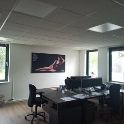 Mariusz Markowski - Wnętrze biura z panelowym sufitem, oświetleniem, biurkami z komputerami i plakatem na ścianie.