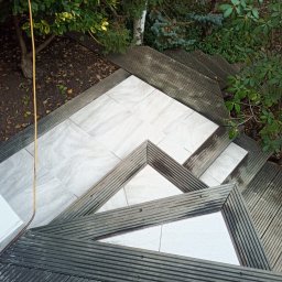 Mariusz Markowski - Zewnętrzne schody z drewnianymi ramami i jasnymi, kwadratowymi płytkami, otoczone zielenią, widok z góry.