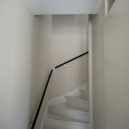 Mariusz Markowski - Klatka schodowa z białymi schodami i czarną poręczą w jasnym wnętrzu, świeżo po malowaniu.
