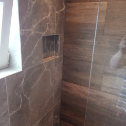 Mariusz Markowski - Ściana kabiny prysznicowej wyłożona brązowymi płytkami imitującymi drewno, sąsiadująca ze ścianą z szarych płytek imitujących marmur z wnęką.