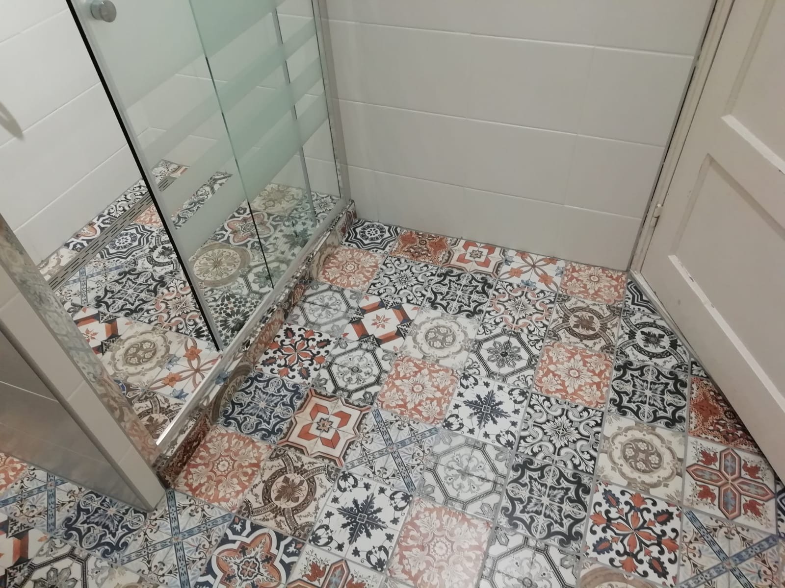 Wzorzyste płytki podłogowe w łazience, ułożone przy kabinie prysznicowej z częściowo matową szybą i białymi płytkami ściennymi oraz drzwiami.