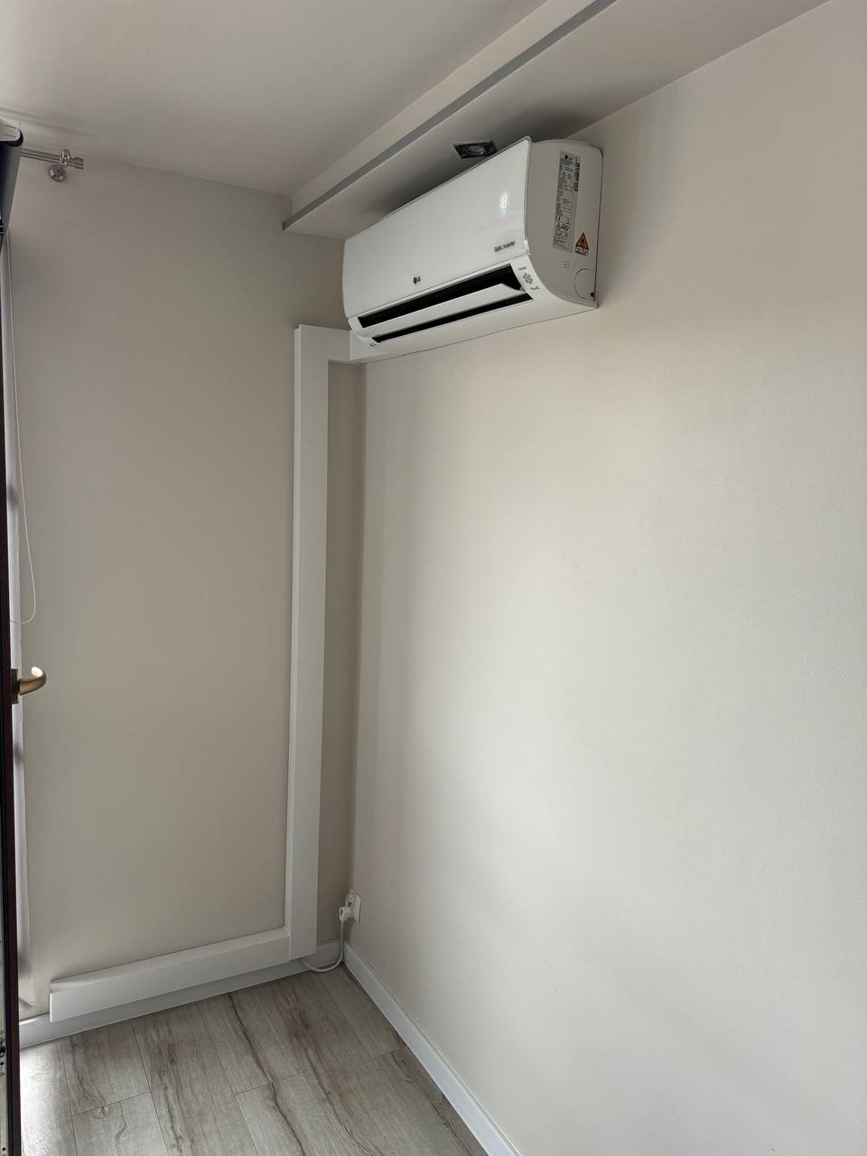 Biały klimatyzator LG zamontowany na ścianie w jasnym pomieszczeniu, widoczna instalacja elektryczna i rurki prowadzone wzdłuż ściany.