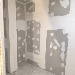 Luckybud - Wnętrze w trakcie prac wykończeniowych: szpachlowane ściany z płyt karton-gips, widoczne łączenia i miejsca po wkrętach, przygotowane do dalszego etapu prac.