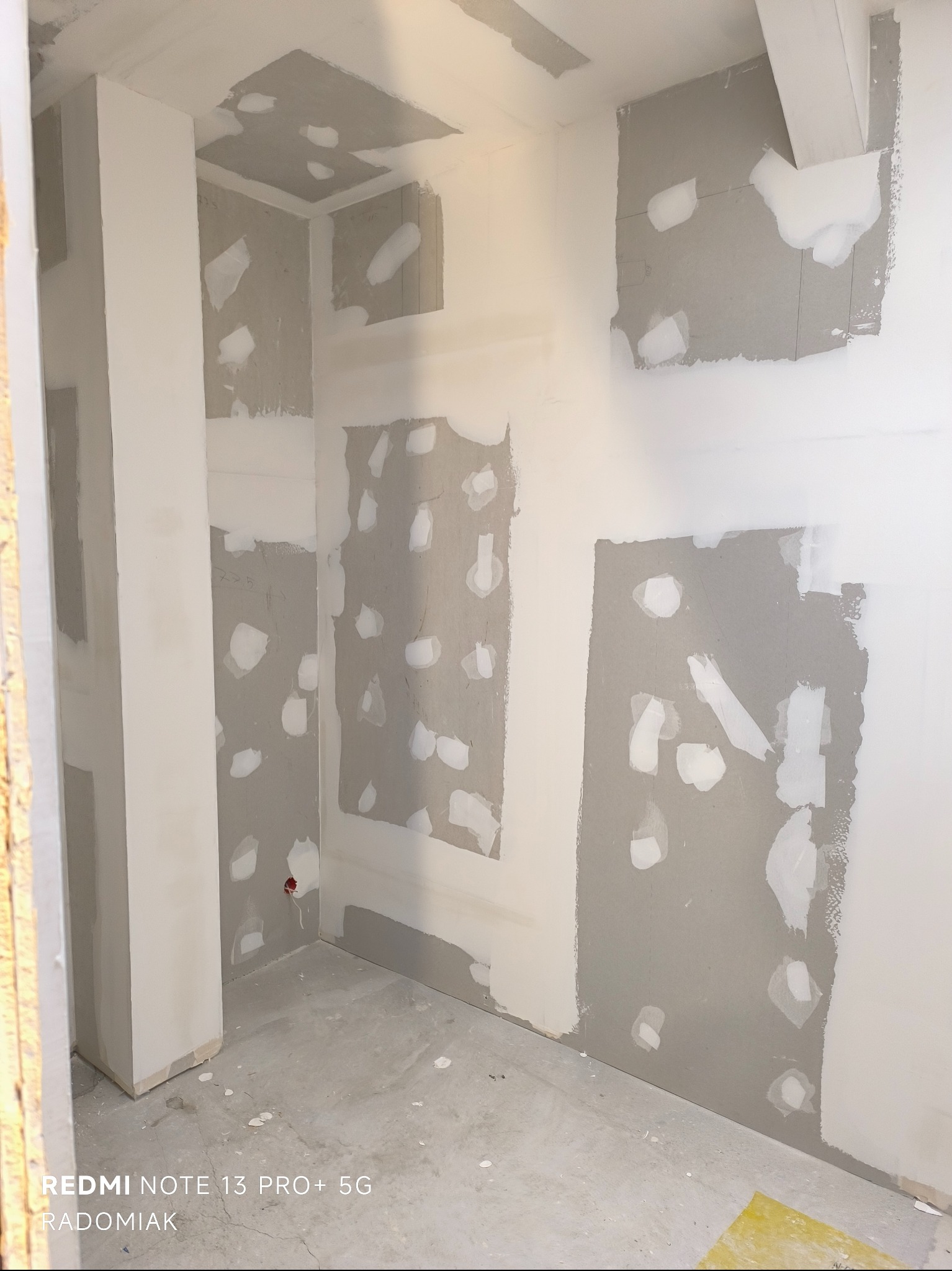 Wnętrze w trakcie prac wykończeniowych: szpachlowane ściany z płyt karton-gips, widoczne łączenia i miejsca po wkrętach, przygotowane do dalszego etapu prac.