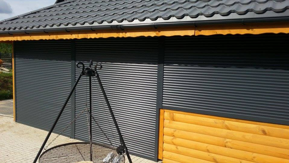 Zewnętrzne rolety w kolorze grafitowym, zamontowane na drewnianej konstrukcji. W tle widoczny grill na trójnogu i dach z szarej blachy.