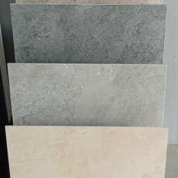 Brillante - Ekspozycja czterech płytek o różnych wzorach i odcieniach szarości oraz beżu, ułożonych jedna na drugiej, prezentujących fakturę i kolory.