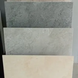 Ekspozycja czterech płytek o różnych wzorach i odcieniach szarości oraz beżu, ułożonych jedna na drugiej, prezentujących fakturę i kolory.