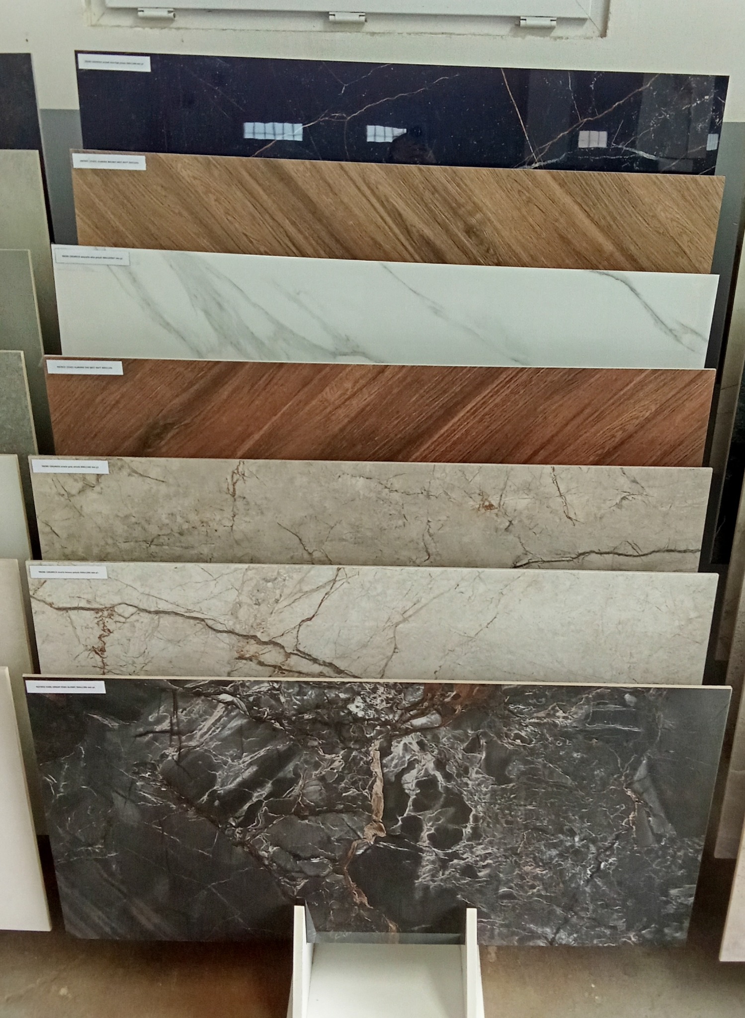 Ekspozycja płytek ceramicznych o różnych wzorach i kolorach, ułożonych warstwowo, prezentujących różnorodność materiałów wykończeniowych do wnętrz.