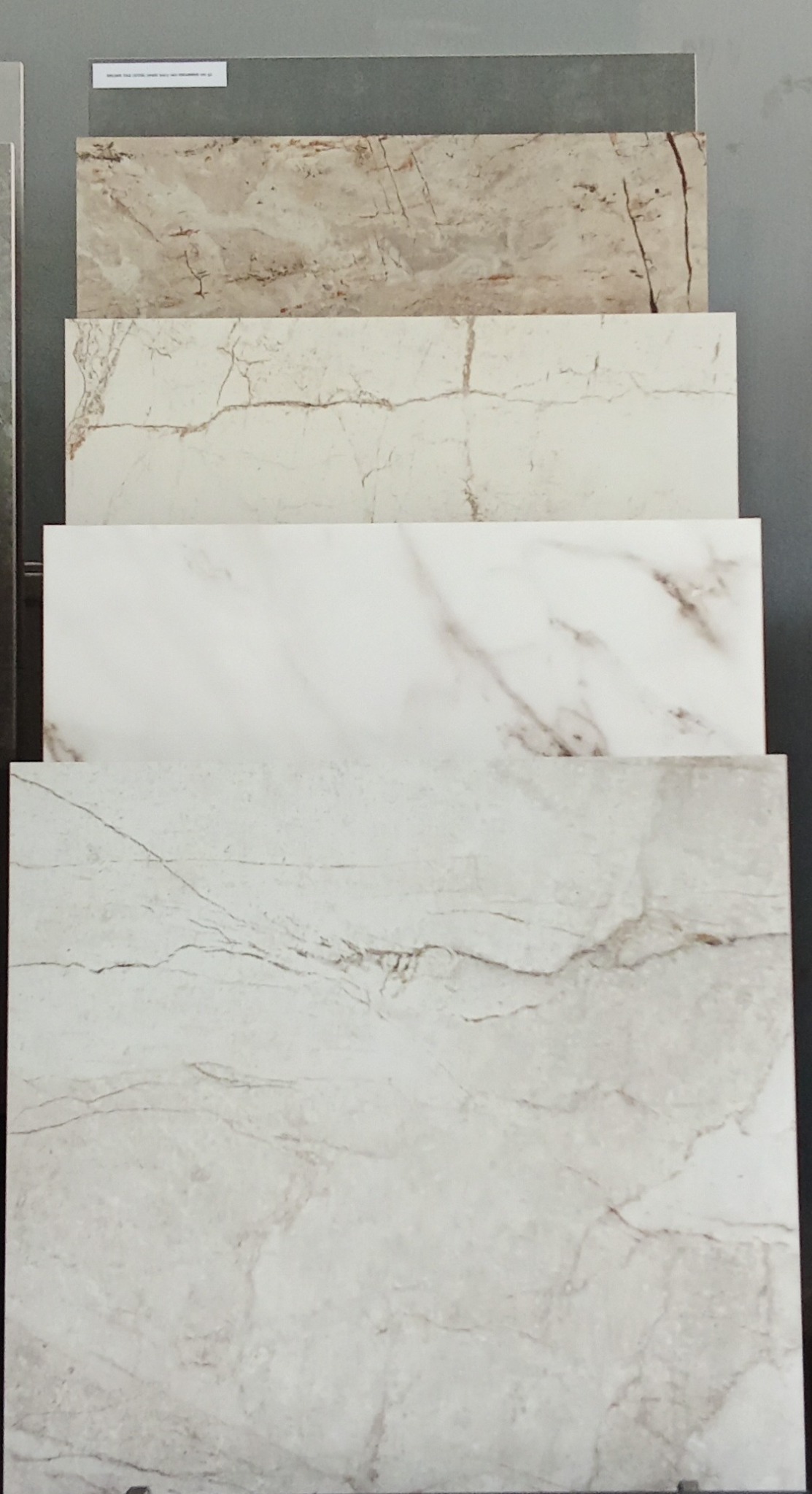 Ekspozycja czterech płytek o marmurowym wzorze w różnych odcieniach beżu i szarości, ułożonych jedna na drugiej, prezentujących fakturę i kolorystykę.