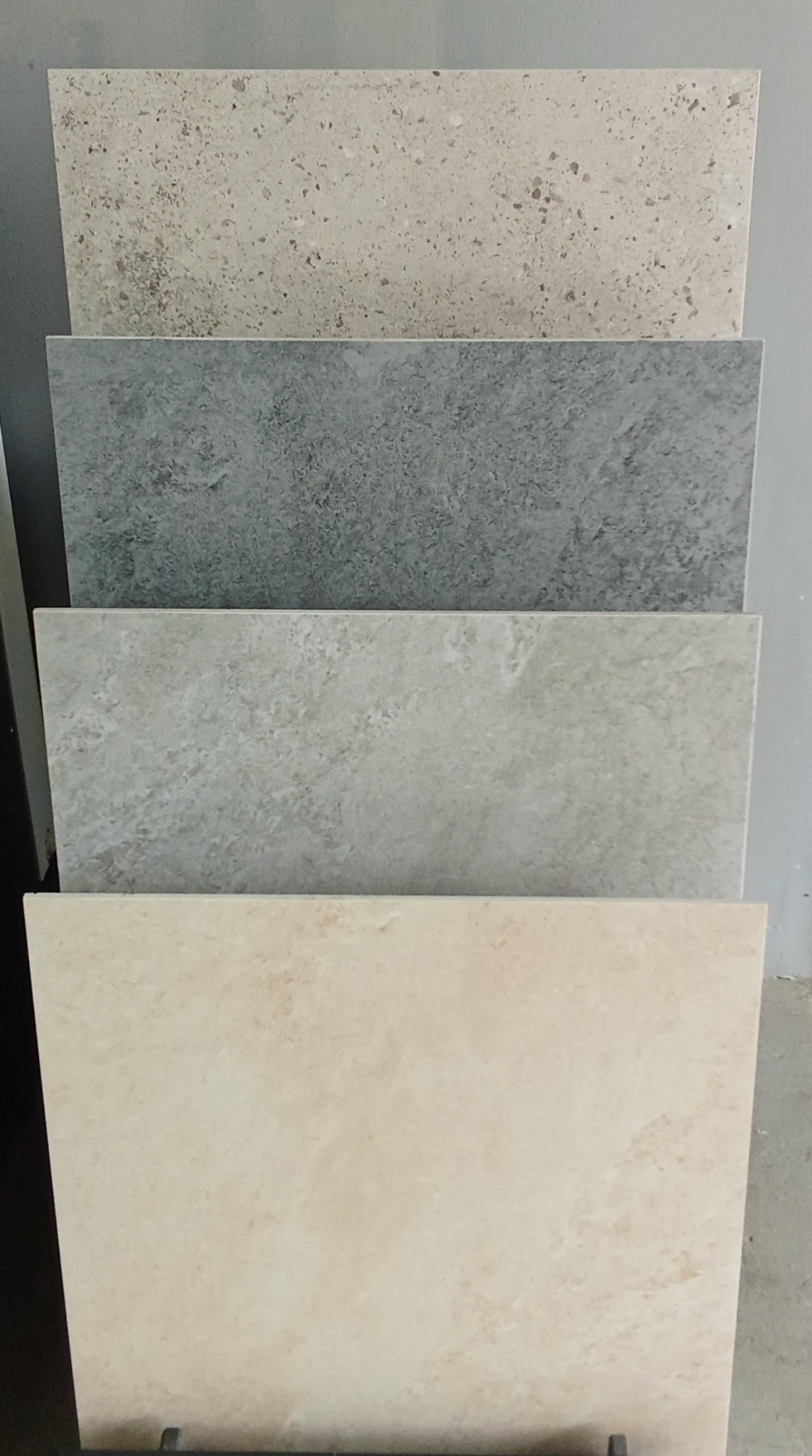 Ekspozycja czterech płytek o różnych wzorach i odcieniach szarości oraz beżu, ułożonych jedna na drugiej, prezentujących fakturę i kolory.