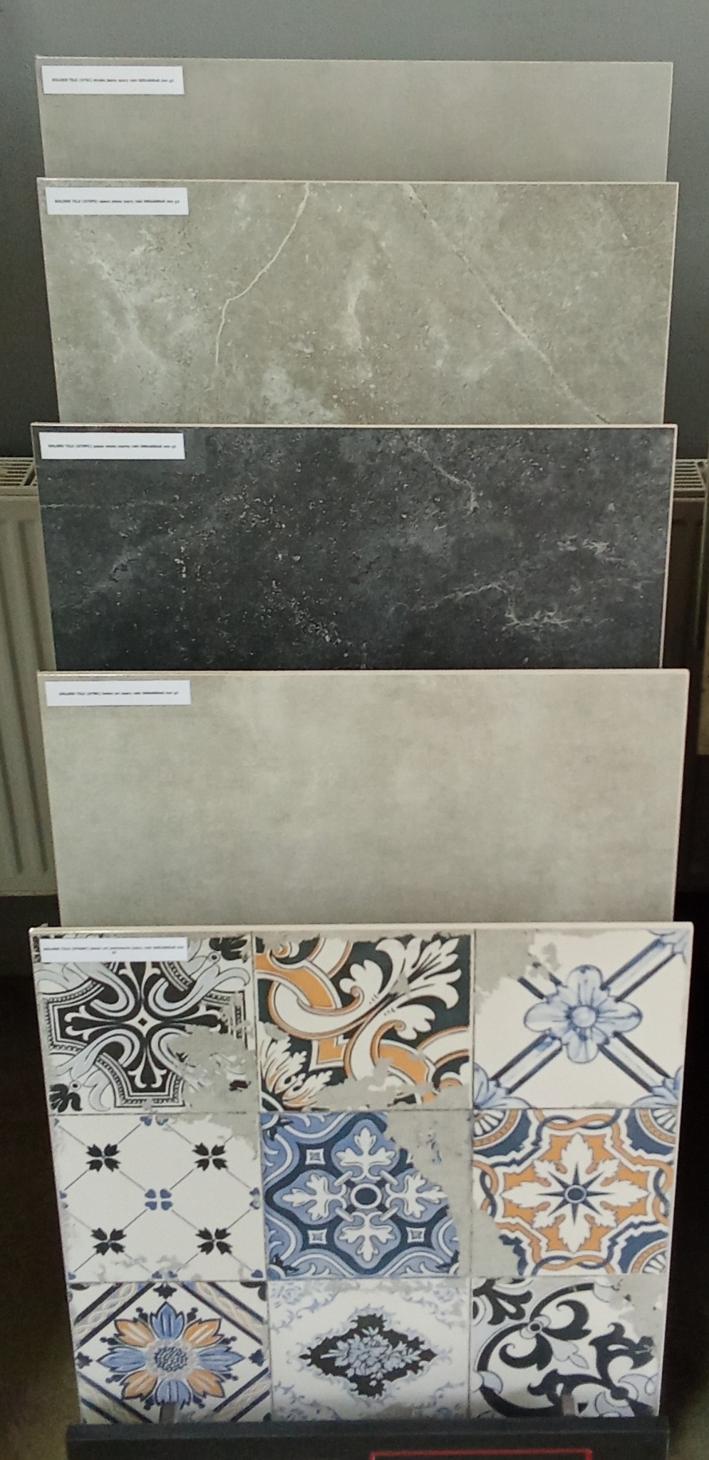 Ekspozycja różnorodnych płytek ceramicznych: gładkie szare, imitujące marmur i wzorzyste patchworkowe, ukazujące bogactwo faktur i deseni.