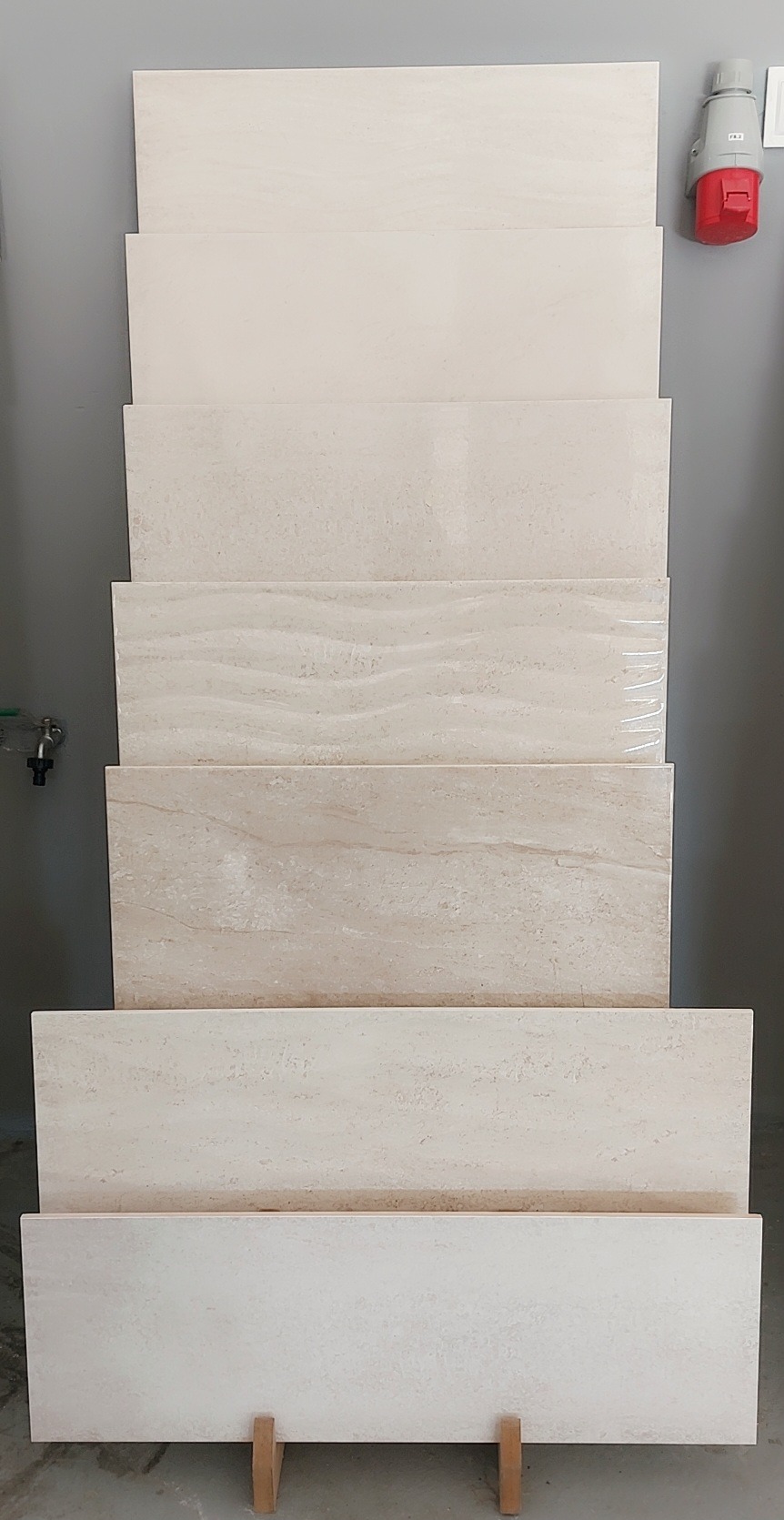 Ekspozycja płytek w odcieniach beżu, ułożonych jedna na drugiej, prezentujących różne wzory i faktury, wspartych na drewnianych elementach.