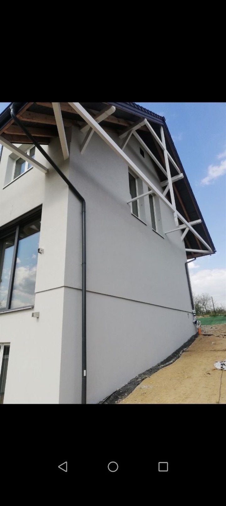 Elewacja domu jednorodzinnego w odcieniach szarości z widocznymi elementami konstrukcyjnymi dachu przed ostatecznym wykończeniem.