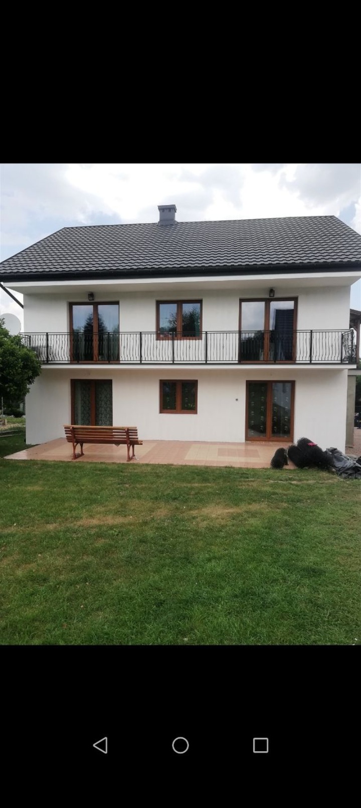 Dwukondygnacyjny dom z balkonami w Zabierzowie po renowacji elewacji. Jasne ściany, ciemny dach, drewniana stolarka okienna i ławka na tarasie.