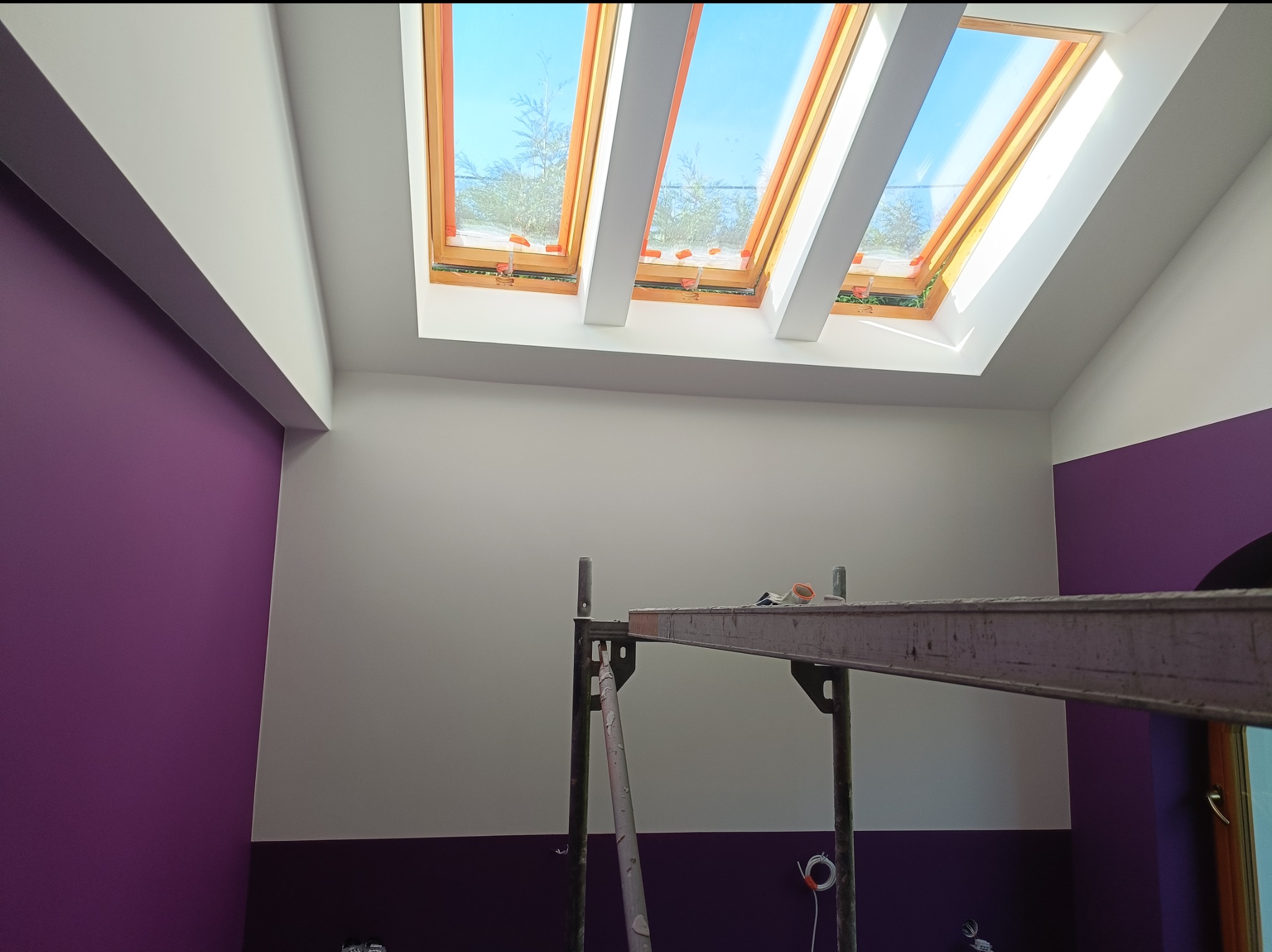 Pokój z fioletowo-białymi ścianami i oknami dachowymi. Widoczny metalowy podest malarski.