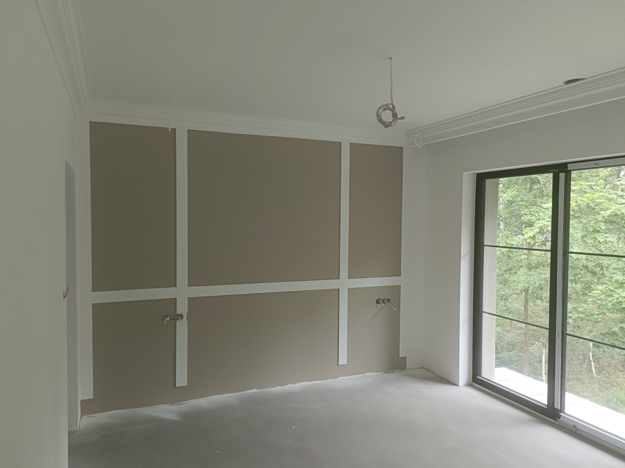 Wnętrze z panelami ściennymi w trakcie montażu, widok na okno z Mińska Mazowieckiego. Detal wykończenia ścian z listwami dekoracyjnymi.