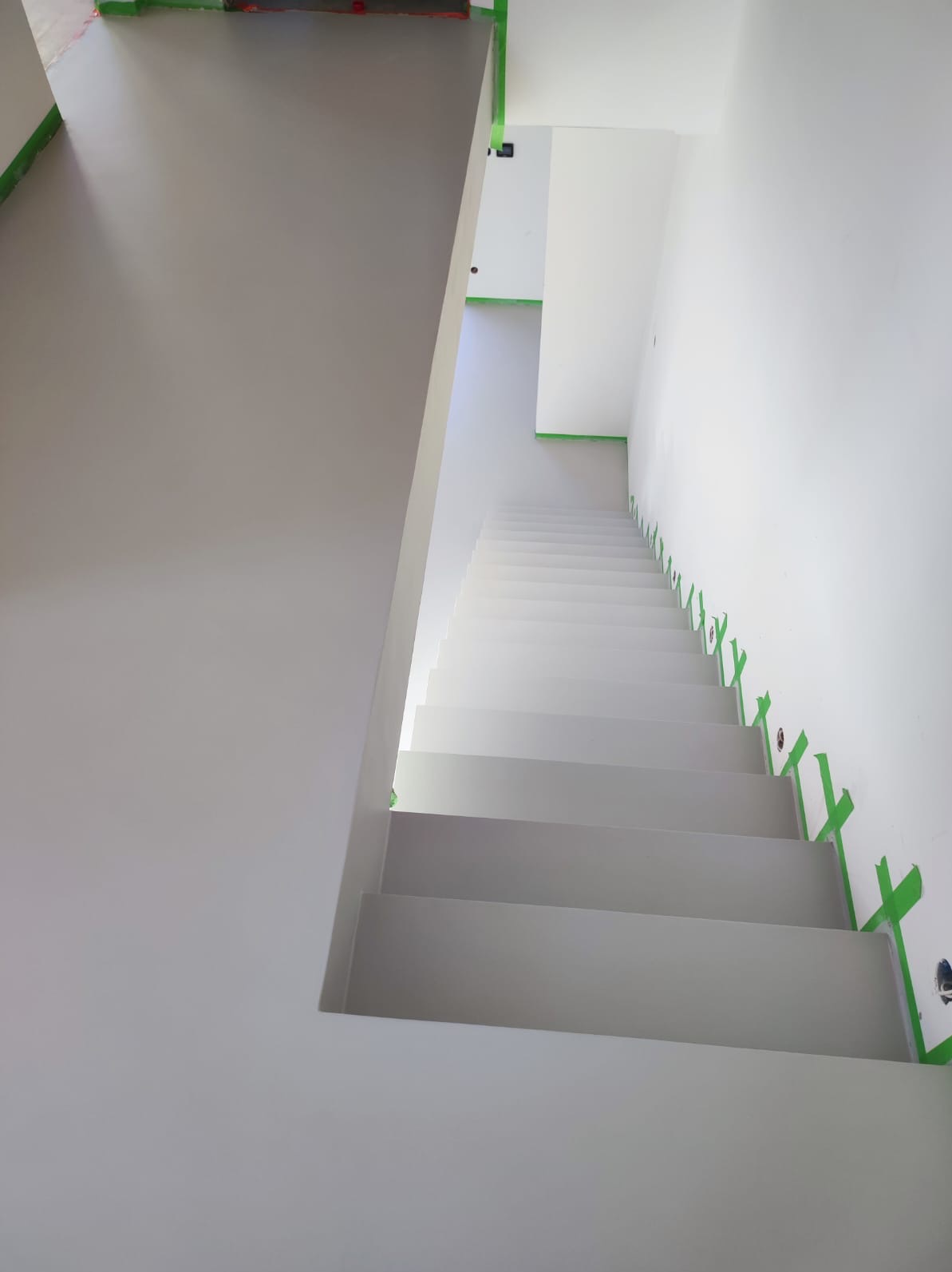 Schody wykończone jednolitą, szarą powłoką, zabezpieczone taśmą malarską, widok z góry.