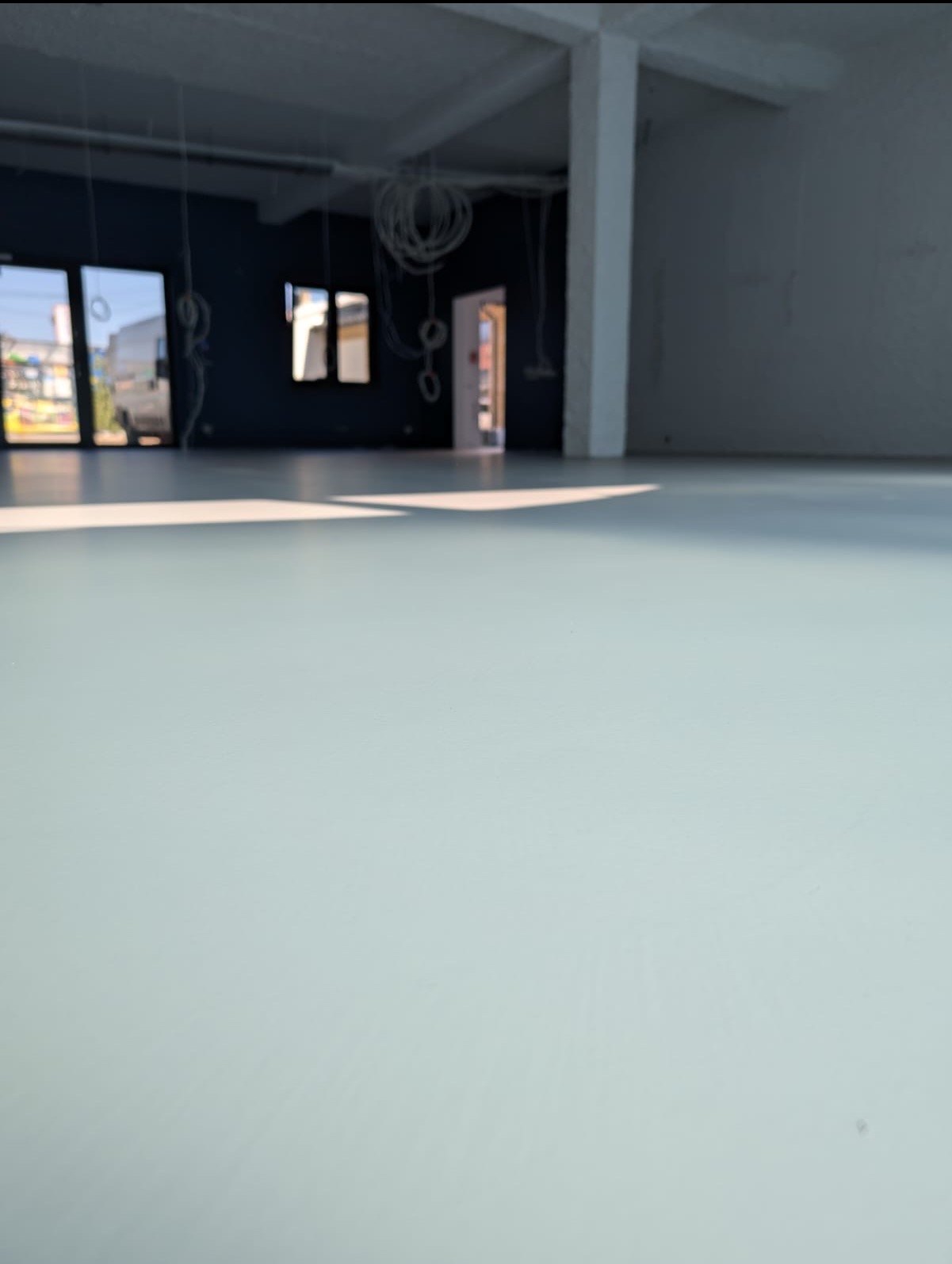 Jasna, gładka posadzka w surowym, industrialnym wnętrzu z widocznymi instalacjami pod sufitem i dużymi oknami w tle.