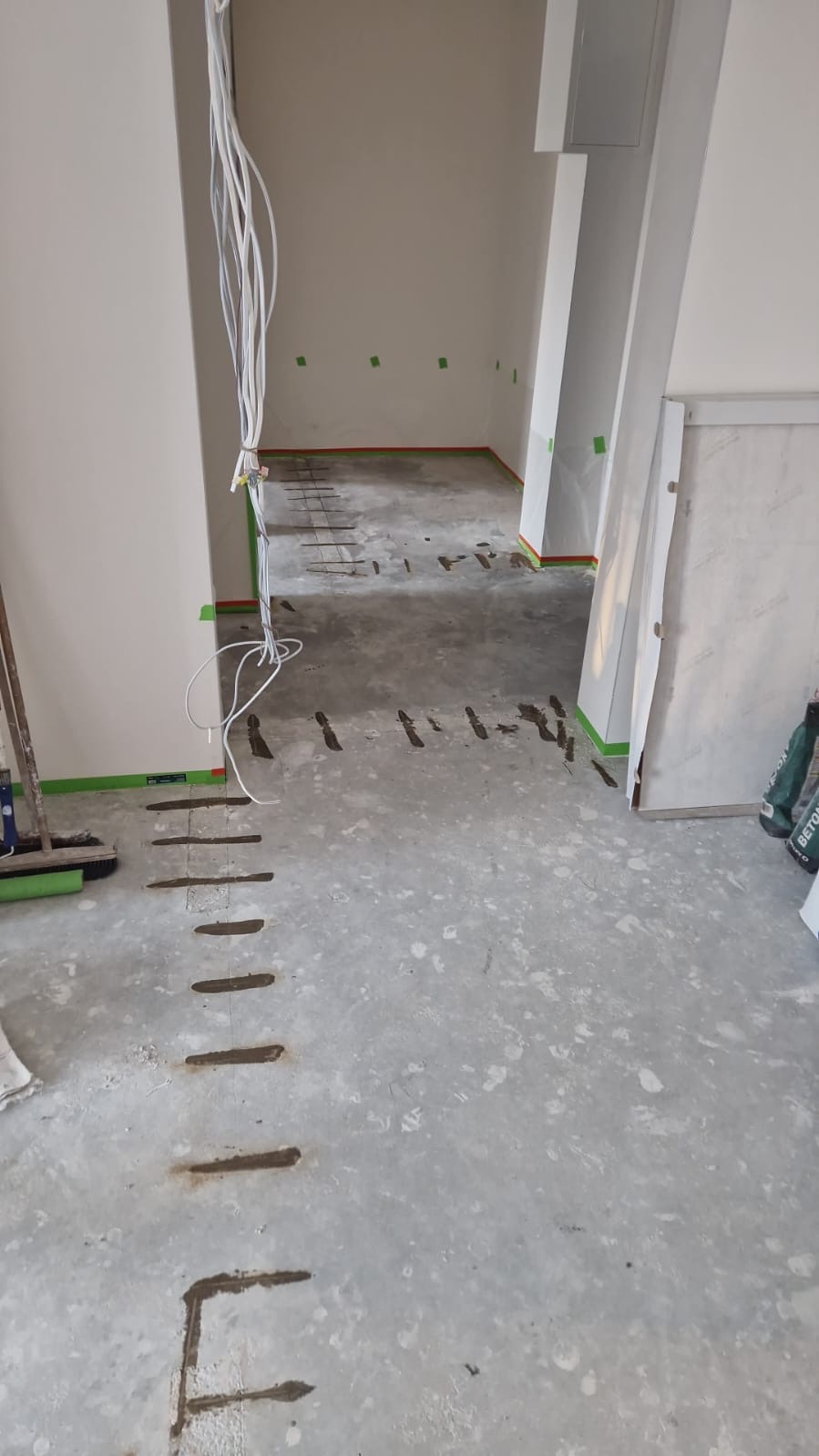 Przygotowanie podłoża pod posadzkę: wywiercone otwory w wylewce, wystające przewody elektryczne, zabezpieczone ściany taśmą malarską.