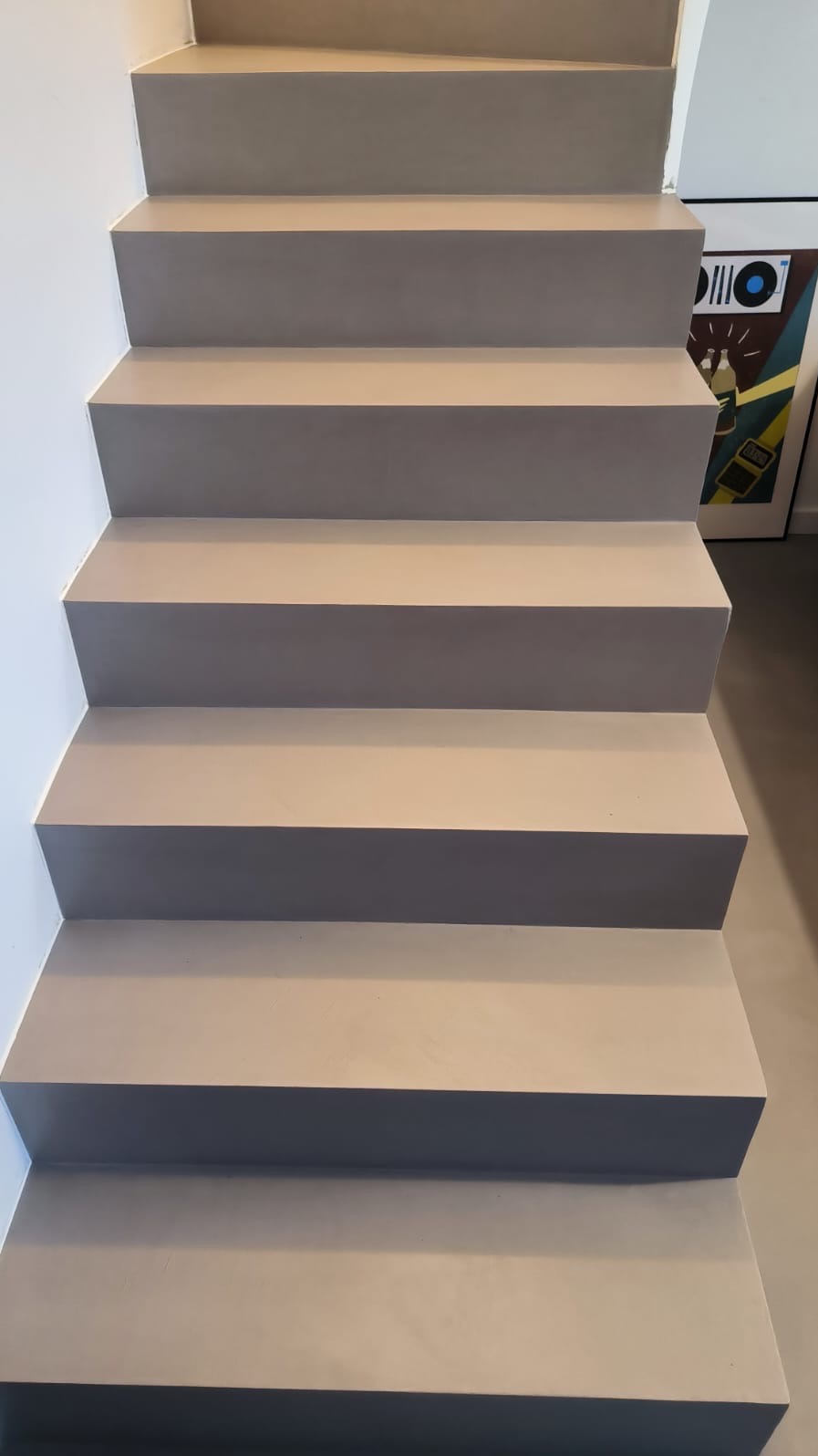 Schody wykończone mikrocementem w odcieniach szarości, widok z dołu, z obrazem w tle. Minimalistyczny design, gładka powierzchnia, nowoczesne wykończenie.