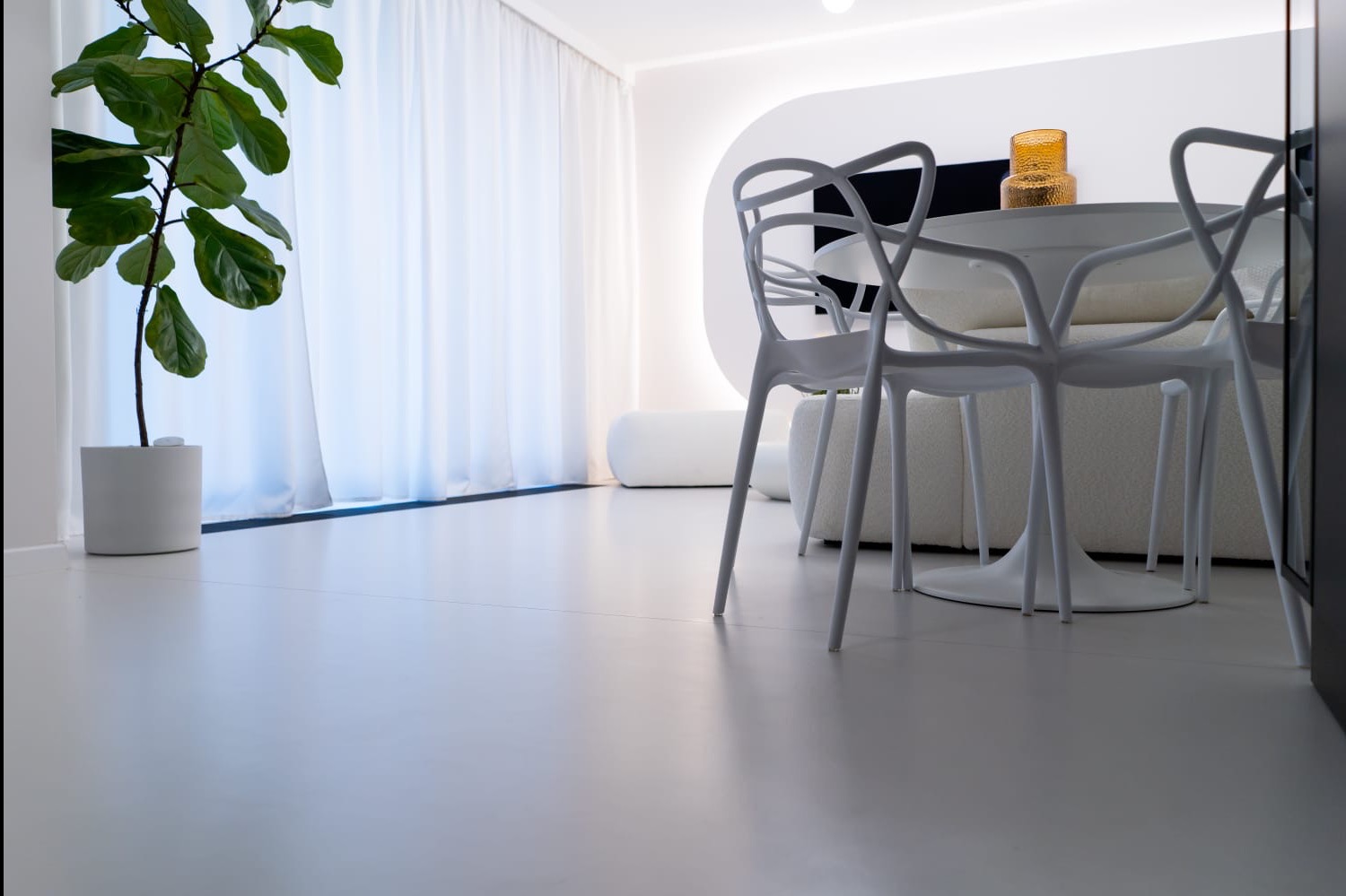 Biała, minimalistyczna posadzka w nowoczesnym wnętrzu z białymi krzesłami i rośliną doniczkową. Gładka powierzchnia podłogi odbija światło, tworząc jasną przestrzeń.