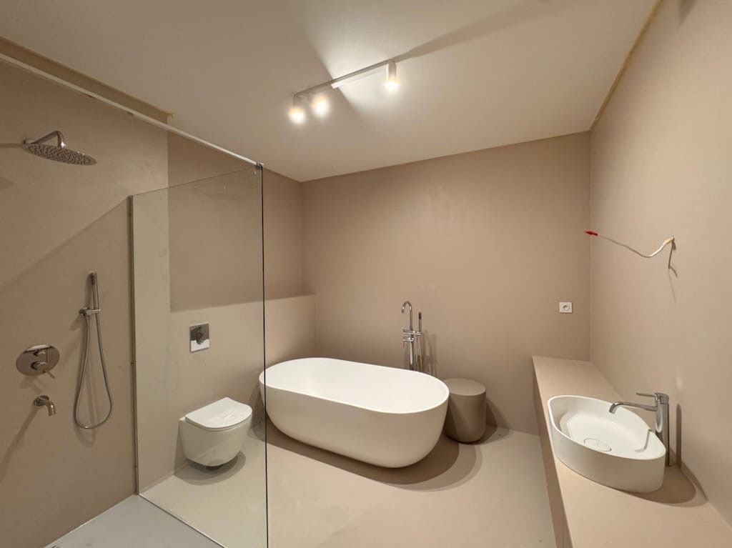 Minimalistyczna łazienka w Lublinie z beżową posadzką, owalną wanną i szklanym prysznicem. Ściany w odcieniach beżu, nowoczesne oświetlenie sufitowe.