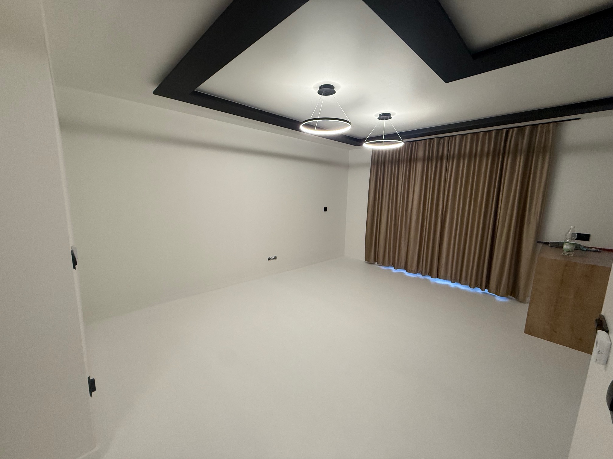 Jasne wnętrze z gładką, jednolitą podłogą i ścianami. Minimalistyczne oświetlenie sufitowe i zasłony w tle. Widok na świeżo wykończone pomieszczenie.