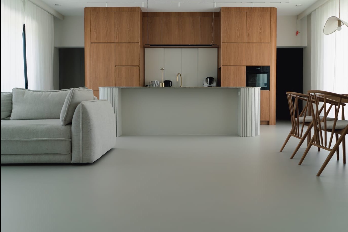 Jasnoszara, gładka posadzka w nowoczesnym wnętrzu z drewnianą zabudową kuchenną i minimalistycznym wyposażeniem. Widoczny fragment sofy i krzesła.