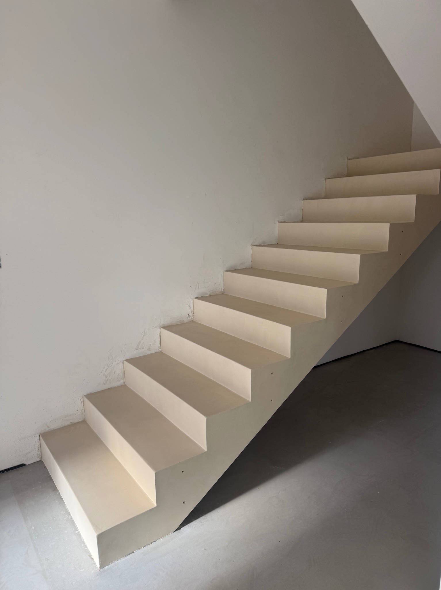 Jasne schody z wykończeniem żywicznym w minimalistycznym wnętrzu. Widoczne detale wykończenia stopni i podłogi. Ujęcie z dołu, podkreślające geometrię schodów.