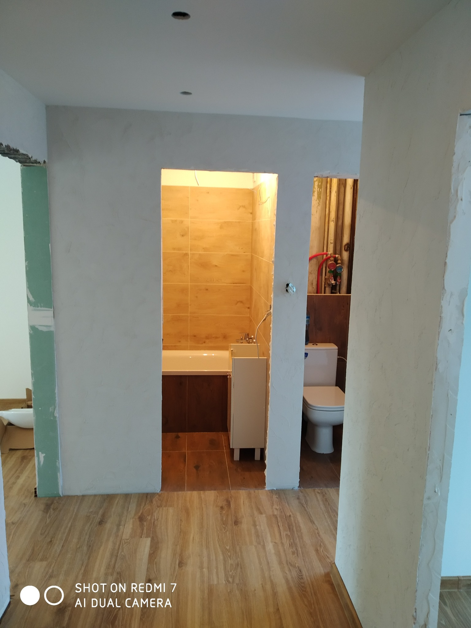 Wnętrze łazienki w trakcie remontu: widoczne surowe ściany, ułożona glazura w kabinie prysznicowej, częściowo ułożona podłoga z paneli, niezagruntowane ściany w korytarzu.