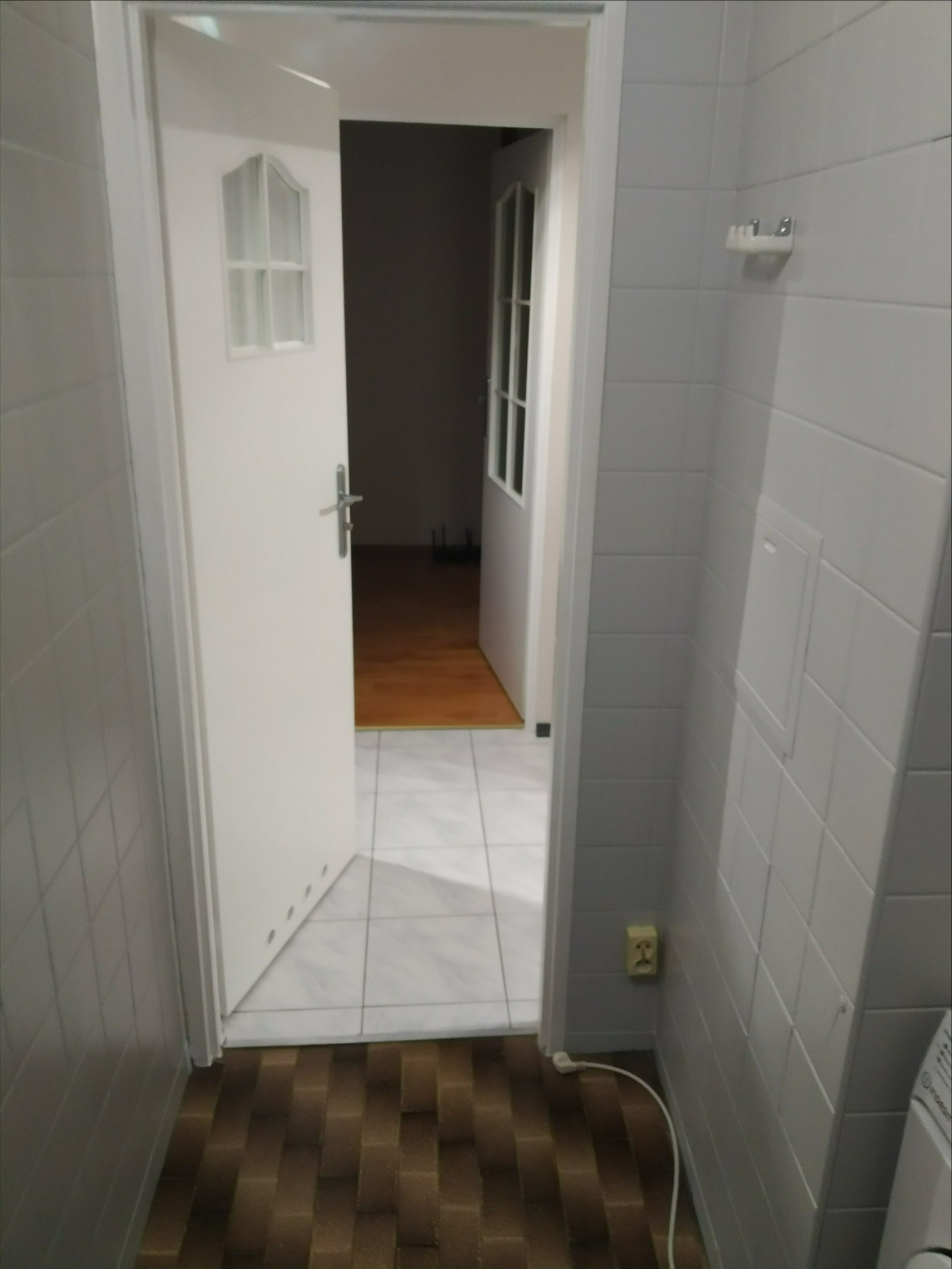 Wykończona łazienka z białą, kwadratową glazurą na ścianach i brązową, prostokątną terakotą na podłodze, z widocznym otwartym wejściem do innego pomieszczenia.