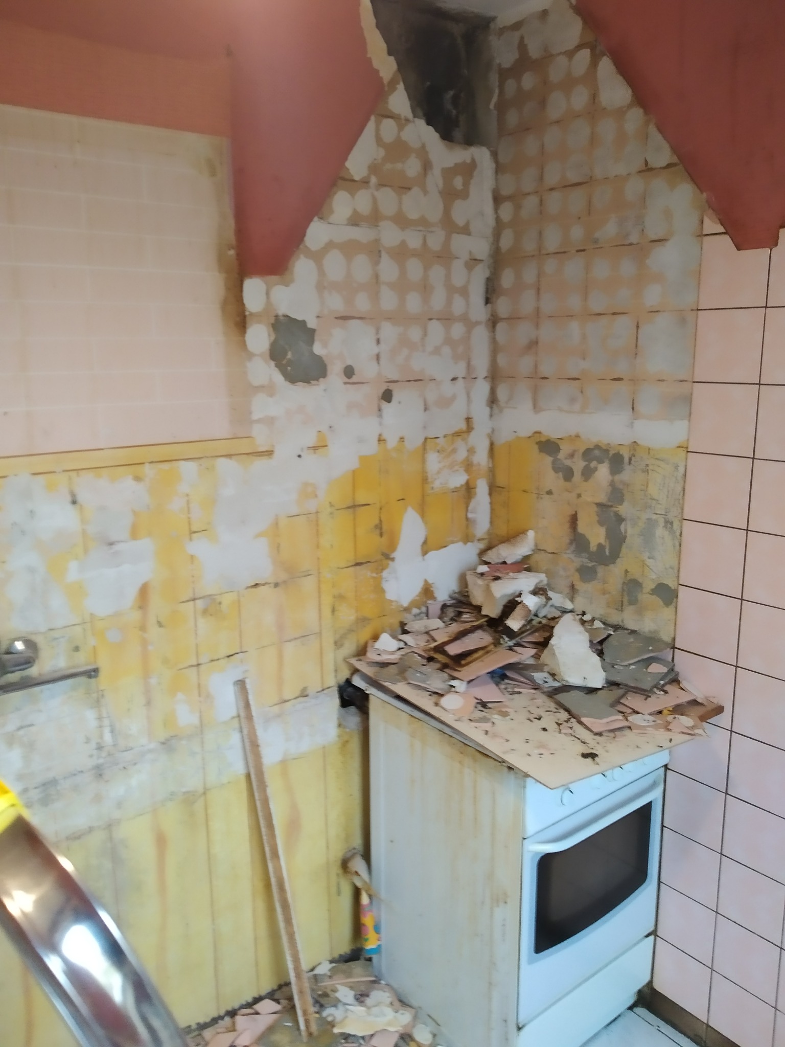 Kuchnia w trakcie demontażu starych płytek, widoczne odsłonięte ściany, resztki kleju i gruzu na kuchence.