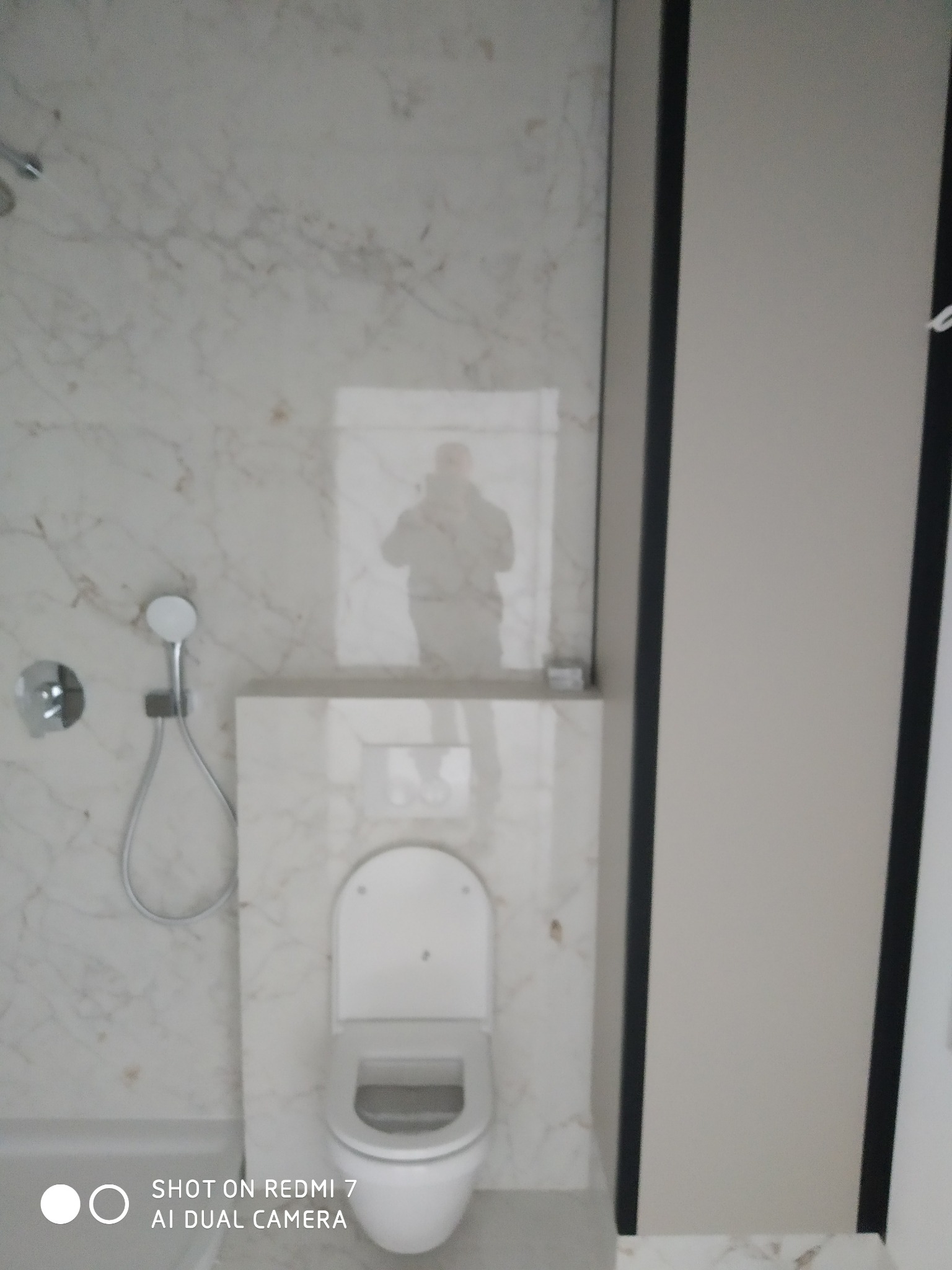 Nowoczesna łazienka wykończona marmurem, z podtynkową spłuczką i minimalistyczną słuchawką prysznicową.