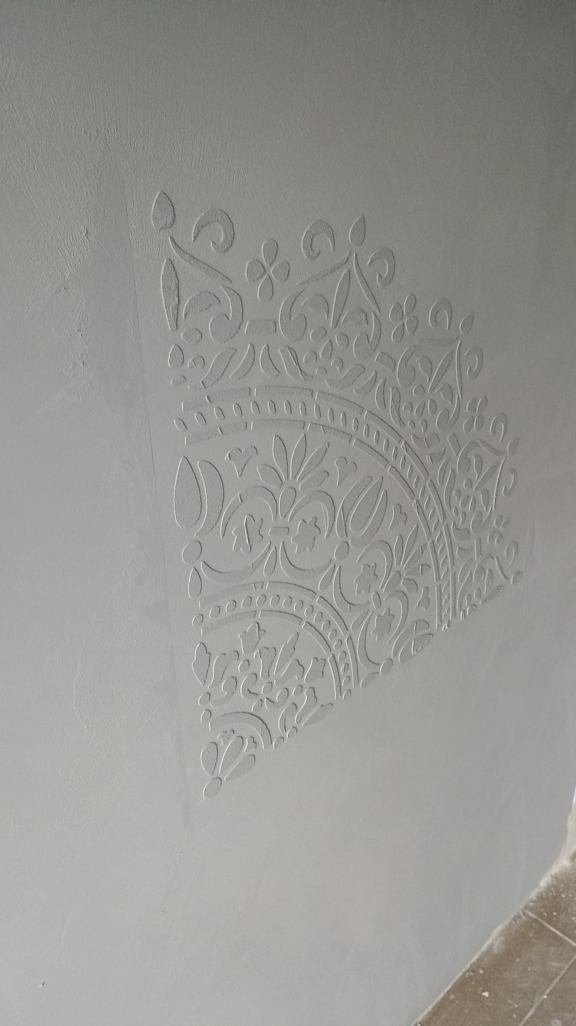 Dekoracyjna płaskorzeźba w rogu ściany, motyw roślinny i geometryczny w jasnym, neutralnym odcieniu.