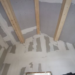 Zakład budowlany - Poddasze z płytami gipsowymi i drewnianymi belkami w Kościanie. Widoczne szpachlowane łączenia płyt. Prace wykończeniowe w trakcie realizacji.