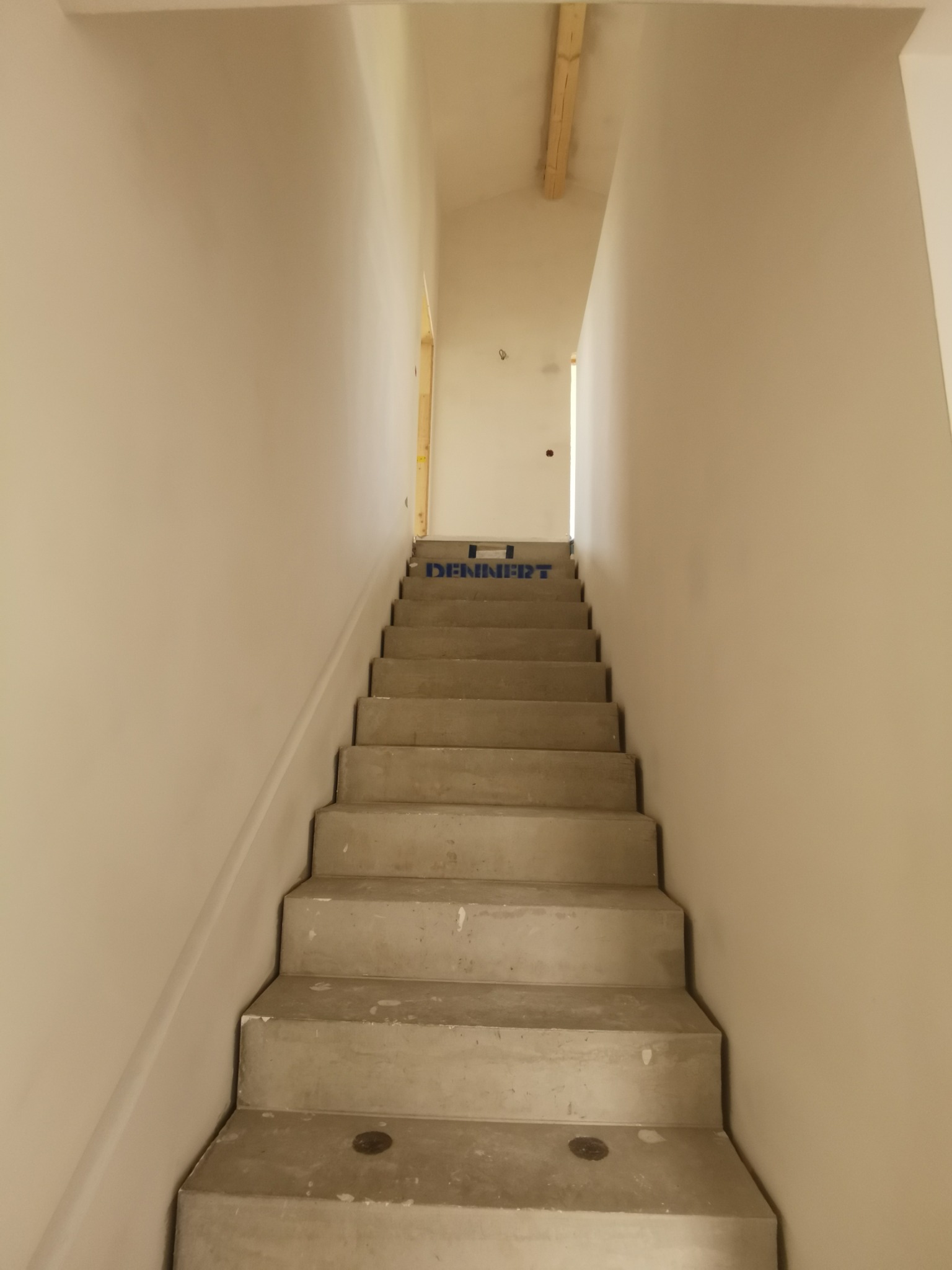 Surowe betonowe schody w trakcie remontu, zabezpieczone niebieską folią ochronną Dennerdt, z widocznymi śladami zaprawy i gładzi na ścianach.