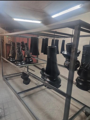 Elementy dekoracyjne lamp ogrodowych zawieszone na metalowym stelażu po malowaniu proszkowym na czarno, widoczny piec do malowania w tle.