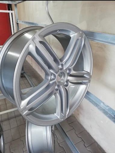 Aluminiowa felga samochodowa po renowacji, zawieszona na metalowym wieszaku, z widoczną gładką, srebrną powłoką.