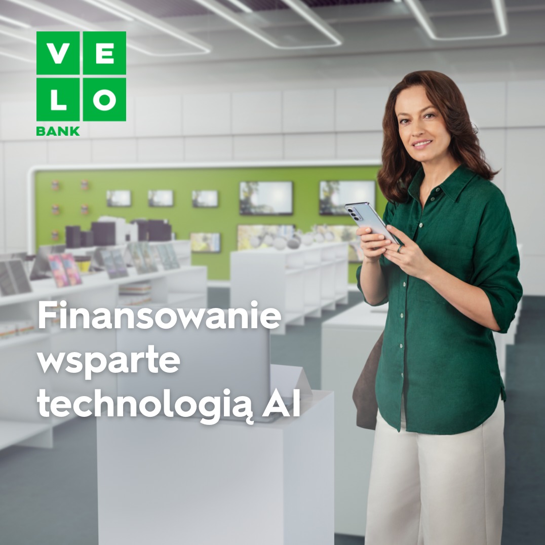 Uśmiechnięta kobieta w zielonej koszuli trzyma smartfon w salonie banku Velo, z napisem 'Finansowanie wsparte technologią AI'.