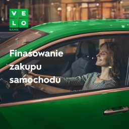 VeloBank S.A. - Uśmiechnięta kobieta za kierownicą zielonego samochodu; w tle logo banku i napis 'Finansowanie zakupu samochodu' na szybie.