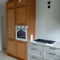 HB STUDIO Hanna Blicharska - Kuchnia z drewnianymi szafkami, białym piekarnikiem marki SMEG i szarą zabudową pod blatem, na którym stoi kuchenka gazowa SMEG oraz rolka ręcznika papierowego.