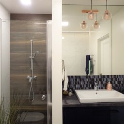 HB STUDIO Hanna Blicharska - Nowoczesna łazienka z kabiną prysznicową i umywalką, lustro odbija wnętrze. Drewnopodobne płytki i szklane lampy dodają elegancji.